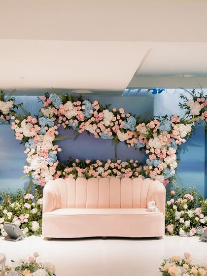 A beautiful pastel stage setup for a Roka ceremony. The backdrop is a soft, painted sky, framed by a cloud of pink, blue, and white hydrangeas and roses, creating a dreamy and romantic atmosphere.