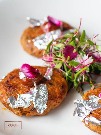 A detailed shot of the Mutton Chapli Kebabs, served with a fresh microgreen salad. The combination of textures and spices makes this a favorite appetizer.