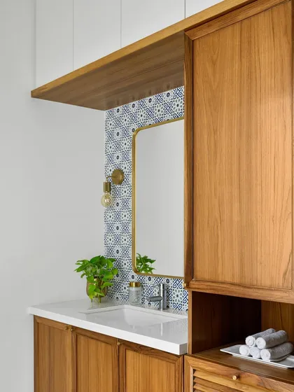 We designed this chic basin niche with integrated storage for laundry essentials. The patterned blue tiles and warm wood create a functional and stylish utility space.