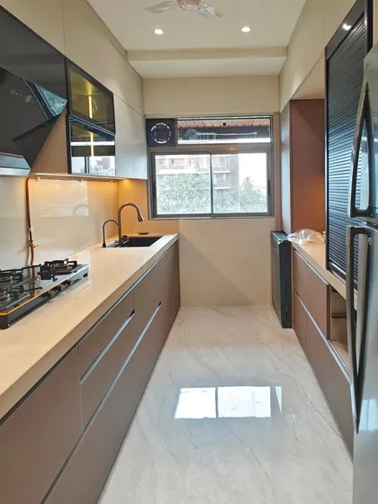 A full-length view of the cappuccino-themed parallel kitchen. The glossy, reflective flooring and handleless cabinets create a spacious and streamlined look, while the window provides ample natural light.