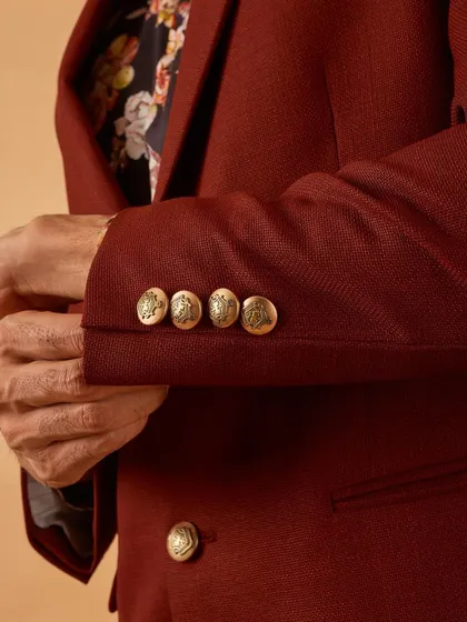 A close-up of the custom-embossed gold buttons on the cuff of the maroon blazer, a small detail that signifies luxury.