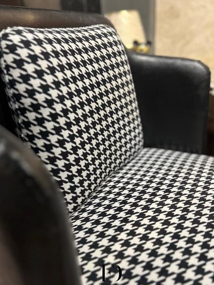 A pair of armchairs that make a graphic statement with a black-and-white houndstooth fabric. Paired with a black leather back and a gold-finished base, they are the definition of modern chic.
