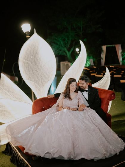 A full-view shot of the couple on their stunning reception stage. The bride's flowing gown and the elegant decor create a fairytale-like scene.