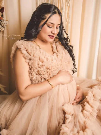 A quiet, tender moment in our Paige gown. The client cradles her baby bump, surrounded by a sea of ruffles.