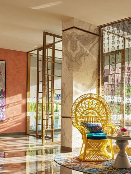 Sunlight streams into this vibrant sitting area at the Taj Devi Ratn. I chose bold yellow peacock chairs and a colorful rug to complement the warm, textured walls and large-scale floral art, creating a cheerful and artistic corner.