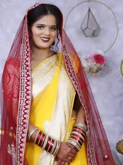 A beautiful bride in a yellow saree and red dupatta, a classic combination for North Indian wedding rituals. The makeup is kept bright and fresh.