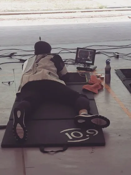 A shooter practices in the prone position, a fundamental aspect of certain rifle events. We coach athletes on body stability and rifle support to maximize accuracy from this position.