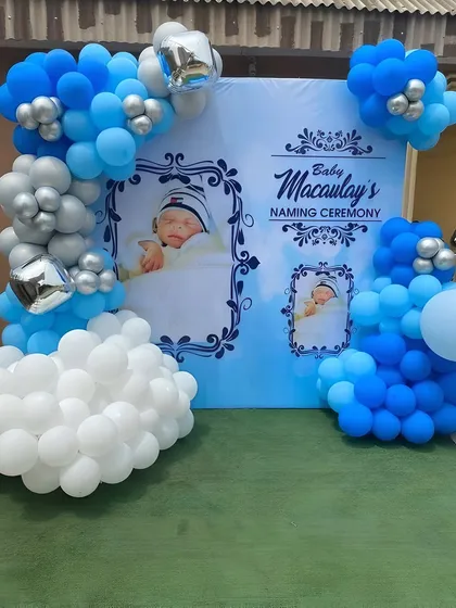 A personalized naming ceremony backdrop in blue and white. The design features photos of the baby, creating a heartfelt and custom touch, framed by a balloon arrangement.
