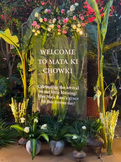 "Welcome to Mata Ki Chowki." For this spiritual gathering, we created a serene and beautiful entrance using a clear acrylic sign adorned with fresh flowers, set against a backdrop of lush banana leaves.
