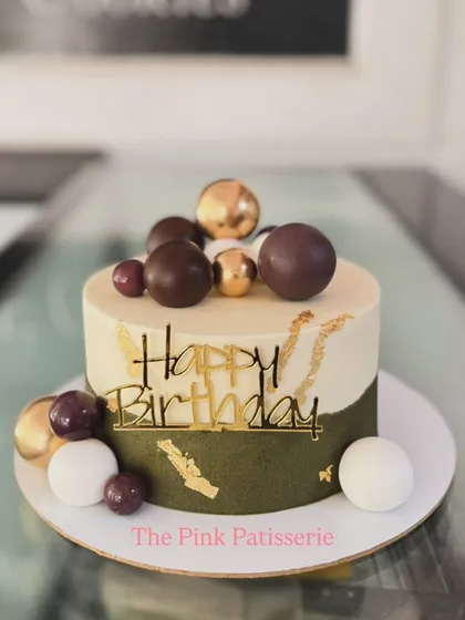 A modern and stylish birthday cake with an olive green and white color block design. It's decorated with chocolate spheres and gold leaf accents.