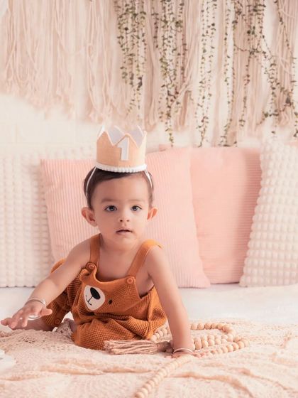 The birthday boy is king for a day! This shot captures his curious expression during his "ONE" year milestone photoshoot in a lovely, warm-toned studio setting.