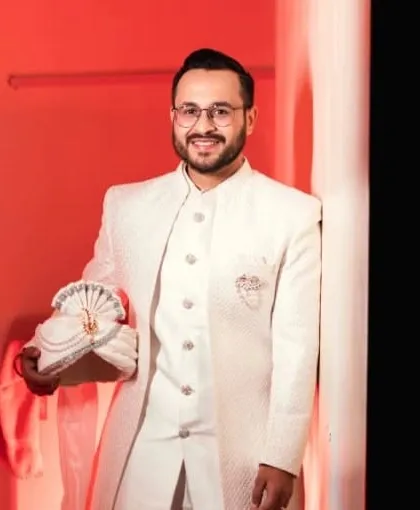 A confident groom holding his turban. The lighting in this shot highlights the smooth, natural finish of the makeup.