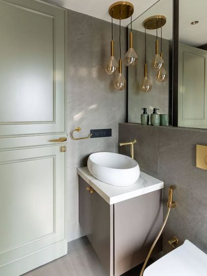 Elevating minimalism with a touch of luxury, this bathroom blends muted sage cabinetry and sleek grey tiles with opulent gold accents. The suspended pendant lights and sculptural sink create a warm, contemporary elegance.