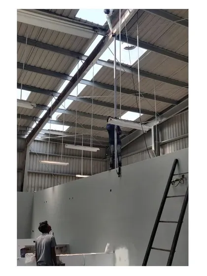 Workers installing lighting fixtures from the high ceiling of the warehouse. This image provides a sense of the scale of the industrial space and the work involved in its completion.