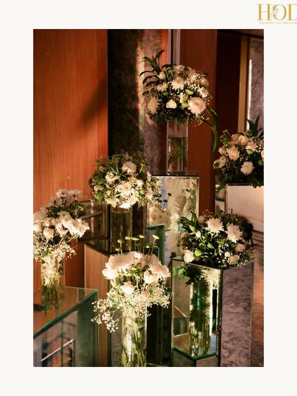 A modern art installation of flowers in glass vases on mirrored pedestals of varying heights, creating a chic and dynamic decor element.