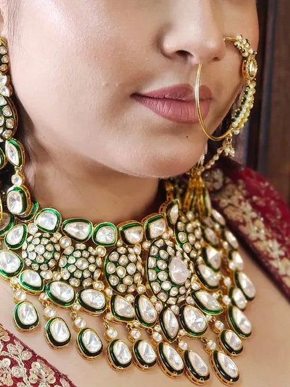 A close-up shot of a heavy Pachi Kundan necklace with green enamel and large uncut stones, paired with a delicate nath.