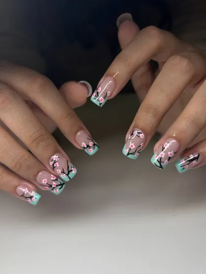 A beautiful cherry blossom nail art design. This set features a mint green French tip with hand-painted cherry blossom branches on a sheer nude base.