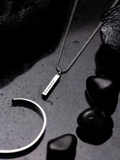 A styled flat lay of a men's silver necklace and bracelet set. The dark, wet slate and stones create a moody and sophisticated atmosphere that elevates the product.