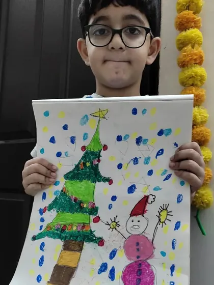 A young artist proudly holds up his cheerful Christmas artwork, complete with a decorated tree and a friendly snowman, made during our holiday session.
