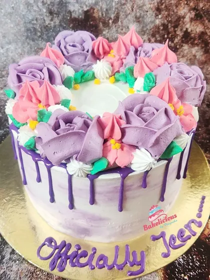"Officially a Teen!" This tall cake features a purple marble effect, a purple drip, and a crown of pink and purple buttercream flowers to celebrate becoming a teenager.
