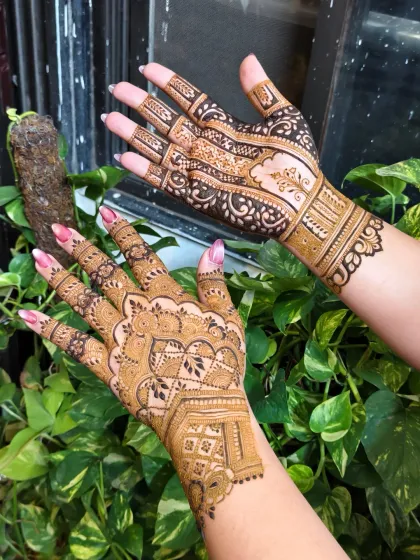 A beautiful bridal design with a mix of bold lines and delicate patterns, seen here against a natural green backdrop that makes the henna stain pop.