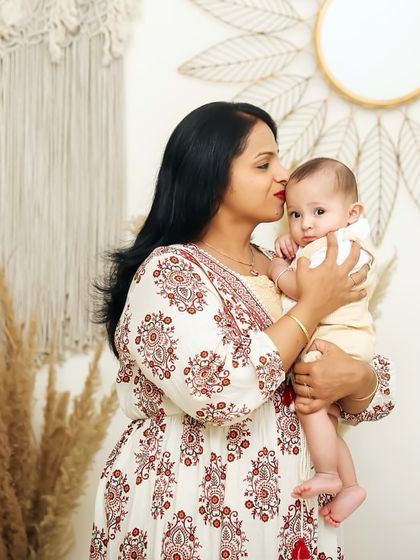 A mother's gentle kiss for her baby. This close-up shot is filled with tenderness and affection, set against a soft, bohemian-style studio background.