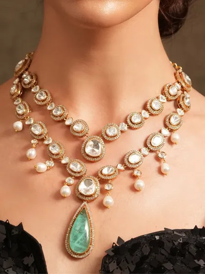 A stunning layered necklace featuring a large emerald drop, designed for a grand statement. The combination of polki and pearls adds a timeless touch.