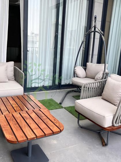 A close-up of the furniture arrangement on the balcony, including a swing chair and lounge seating. The adjustable wooden coffee table adds a layer of functionality to the stylish setup.