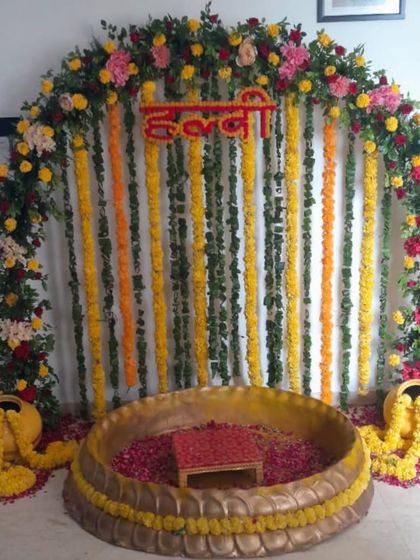 A classic Haldi setup with a full arch of marigolds and other colorful flowers. The large brass urli is filled with rose petals, creating a beautiful and traditional focal point.