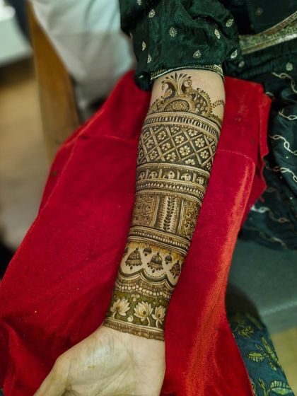 A single arm view of a classic bridal mehendi, showcasing bands of different traditional patterns from the wrist to the elbow.