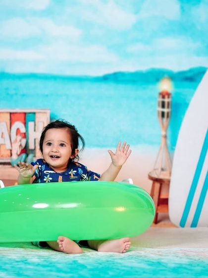 All of God’s grace in one tiny face. A happy baby waves from our fun and colorful beach-themed studio setup.
