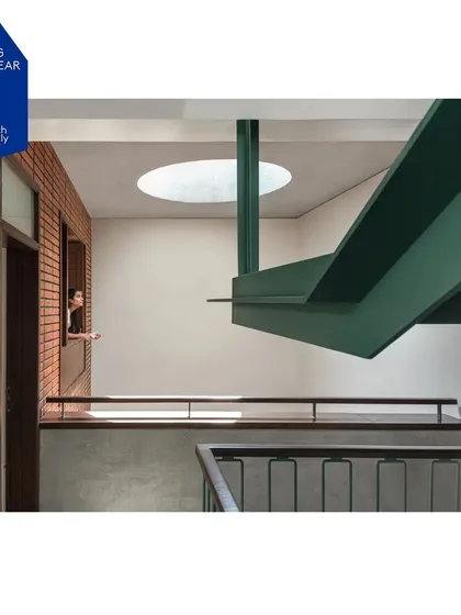 This interior view highlights the interplay of form and light. The strong geometric lines of the green steel staircase are juxtaposed with the soft, diffused light entering from a circular oculus in the ceiling, creating a moment of architectural poetry.