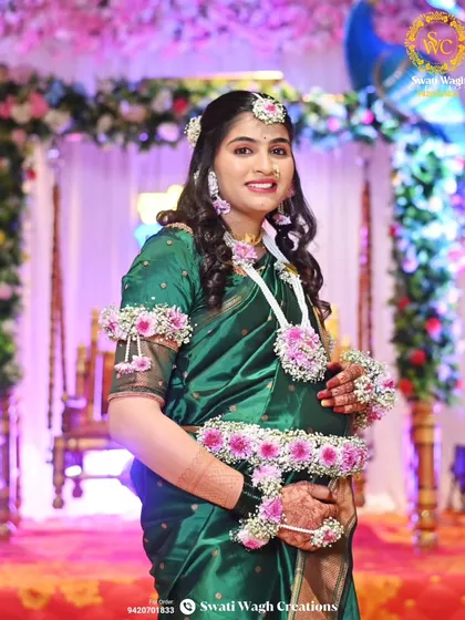 A smiling portrait of the mom-to-be. The floral set includes a maang tikka, earrings, necklace, kamarband, and bajuband.