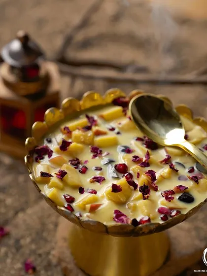 Another view of the Fruit Custard, with a spoon ready to dig in, showcasing its creamy texture and colorful fruit pieces.