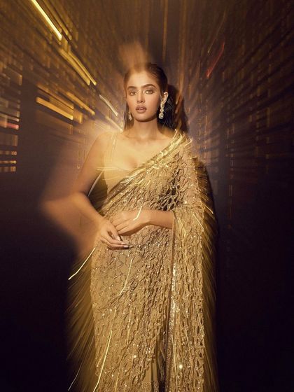 An artistic shot of a glamorous gold saree. The makeup is kept soft and glowing to create a sense of movement and light in the photo.