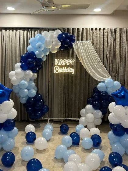 A beautiful blue and white birthday arch with a sheer curtain drape and star-shaped foil balloons.