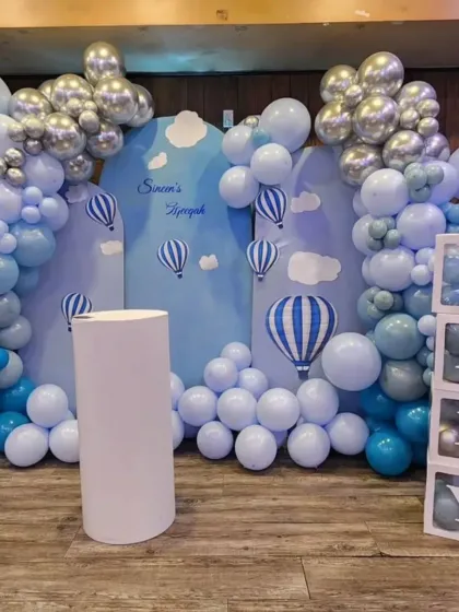 A dreamy hot air balloon themed baby shower. The light blue backdrop with cloud and balloon graphics is framed by a blue and silver balloon arch, creating a serene and beautiful setting.