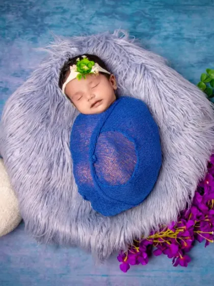 A little prince in blue. This swaddled baby rests on a fluffy bed of fur, surrounded by regal purple flowers.