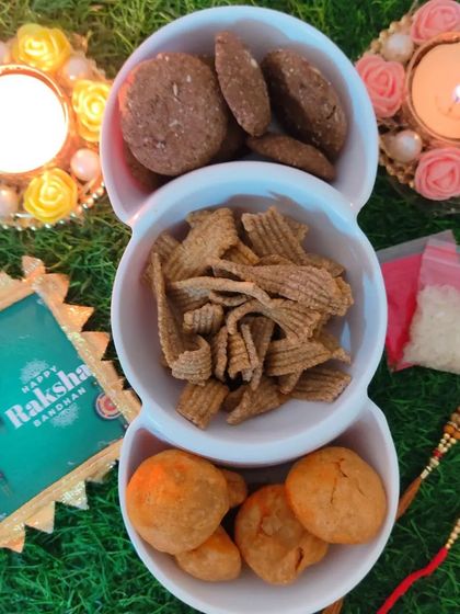 A close-up of our healthy and tasty Rakhi snacks, Ragi Cookies, Ragi Chips, and Khasta Kachori, presented with decorative diyas.