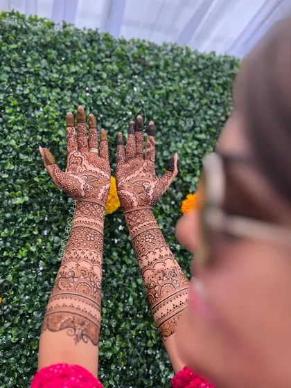 An over-the-shoulder view of a bride's full mehendi, showing the beautiful flow of the design from her palms to her forearms.