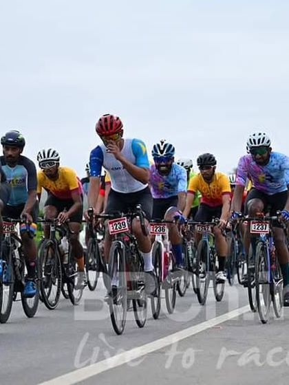 A rider gestures while in the pack, likely communicating with teammates or reacting to the race dynamics.
