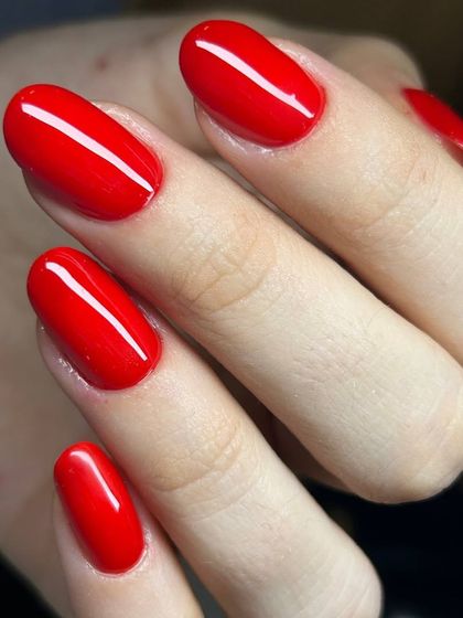 A classic, bright red manicure on oval nails. The color is vibrant and the application is perfectly smooth, showcasing a timeless look.
