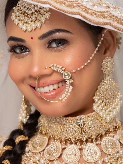 A smiling bride wearing a classic white and gold jewellery set, including a choker, nath, and oversized jhumkas.