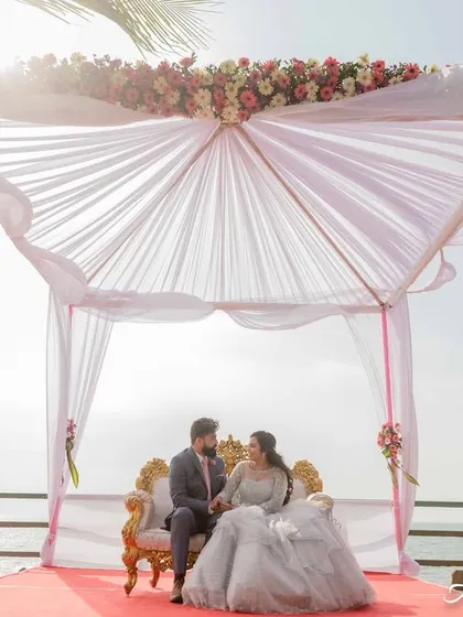 A wide-angle shot of a couple seated under a beautiful canopy by the sea. This photo establishes a sense of place and the grand, romantic setting of their shoot.