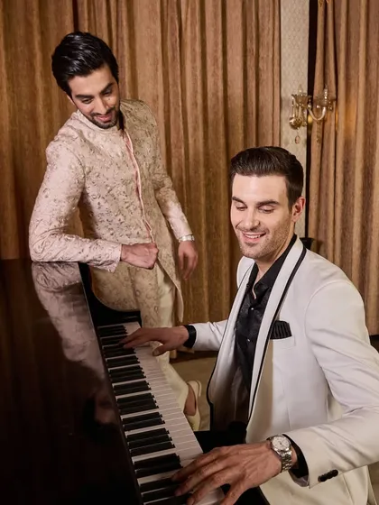 A candid moment showcasing two distinct styles for a celebration. The guest in the tuxedo and the one in the sherwani both look elegant and perfectly dressed for a sophisticated evening event.