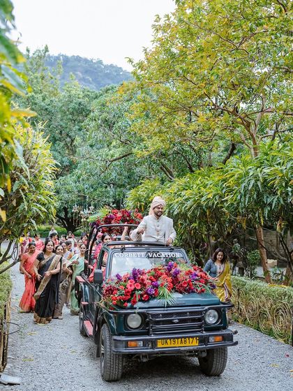 The groom's grand entrance in a flower-adorned jeep, leading his baraat through the forest path in Jim Corbett.