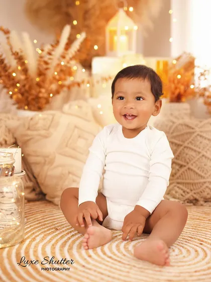 A happy baby boy sitting on a jute rug in our boho-themed studio, surrounded by the warm glow of fairy lights.