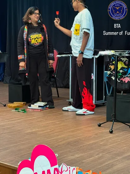 A sweet moment from our Mother's Day magic show, where a young magician presents a flower to an instructor wearing a "Super Mom" shirt.