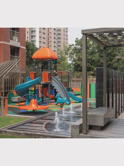 A small water feature and shaded seating are placed adjacent to the play area, allowing for comfortable supervision and sensory play.