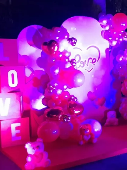 A "LOVE" themed stage illuminated with purple and red lights, featuring light-up letter blocks and heart-shaped foil balloons for a dramatic and romantic effect.